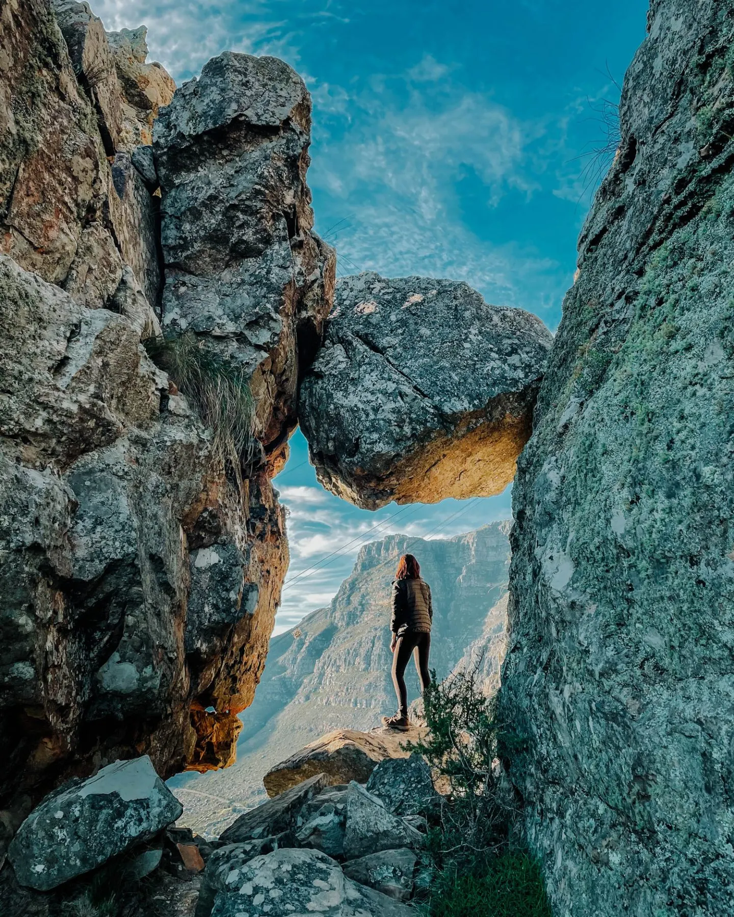 A hiker standing in a rock window on Table Mountain’s India Venster route, with the city and cableway visible far below