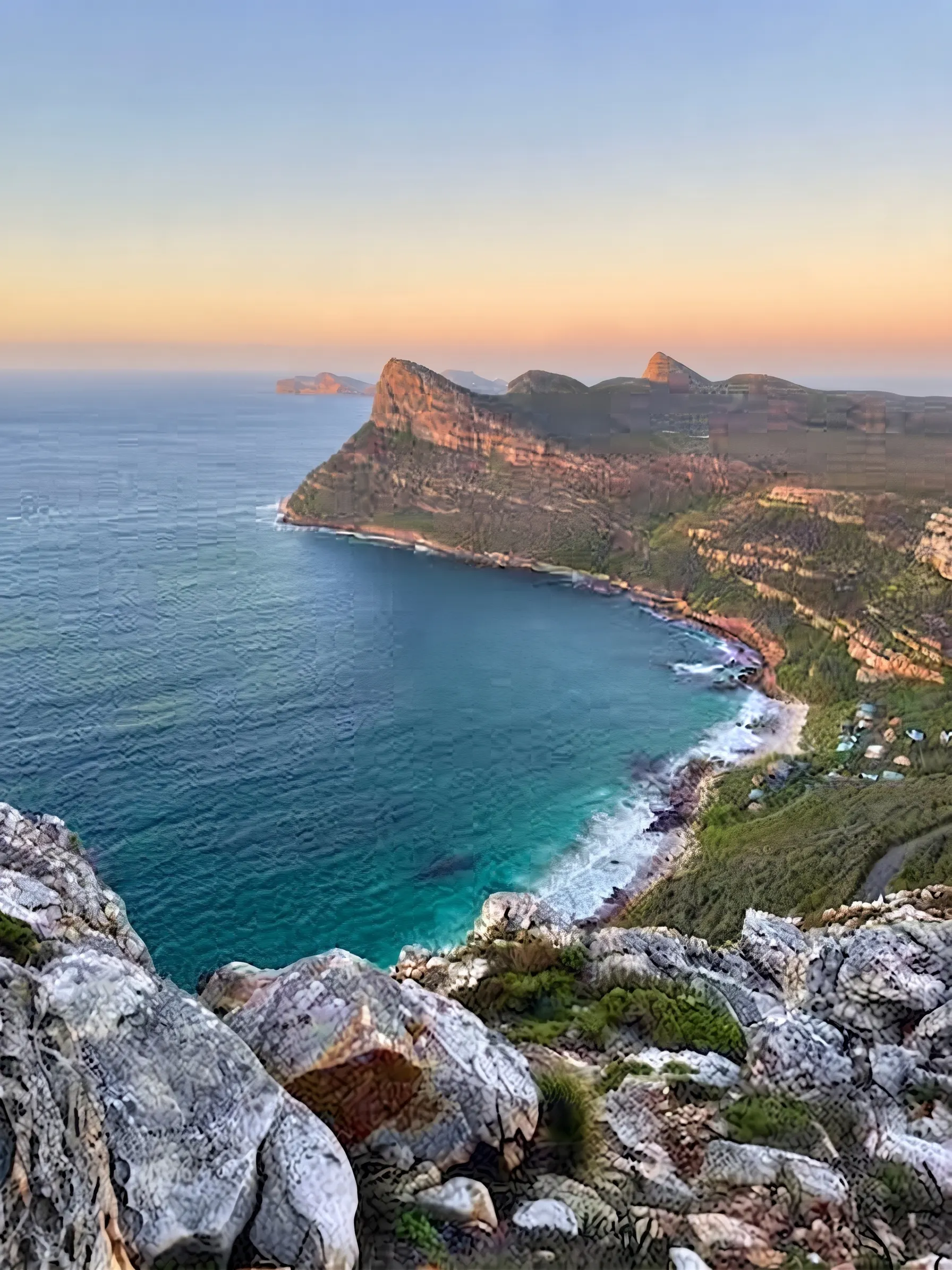 A sunset view down onto Smitswinkel Bay from the trail above, with the rocky Cape Point coastline curving into the distance